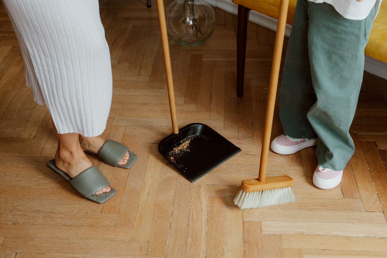 gallery-02 A mother and child cleaning the floor with a broom and dustpan indoors.